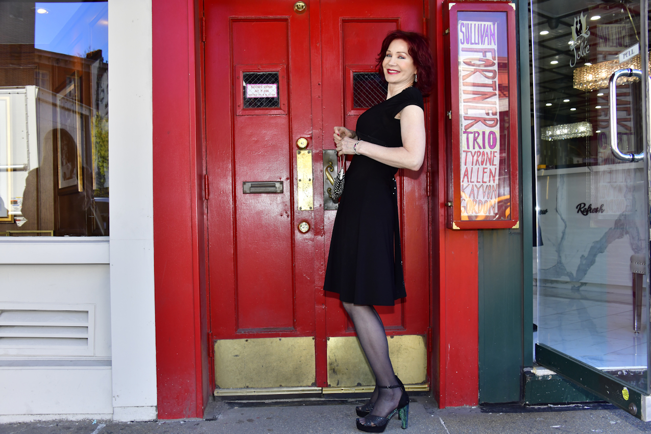 6. Karen Rempel leans against the Village Vanguard’s customary, beloved hand-lettered sign showing the names of the current week’s jazz performers.